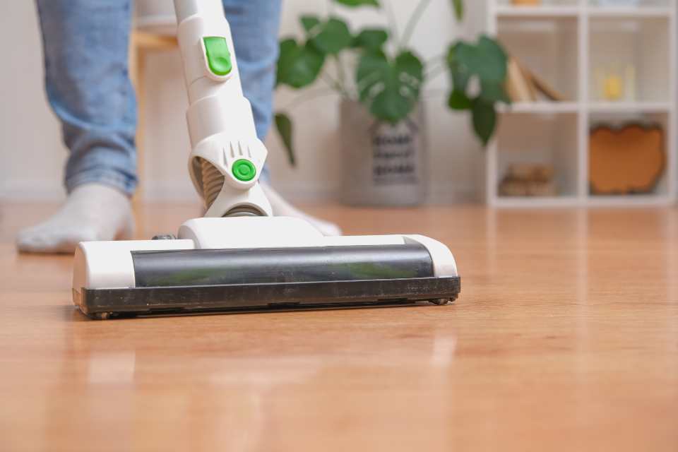 vacuuming a wood look vinyl floor in living room with bookshelf and plant